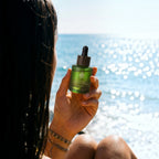 L'Arbre de paix Douceur d'Abricot signature oil in a green glass dropper bottle held against a sunny ocean backdrop