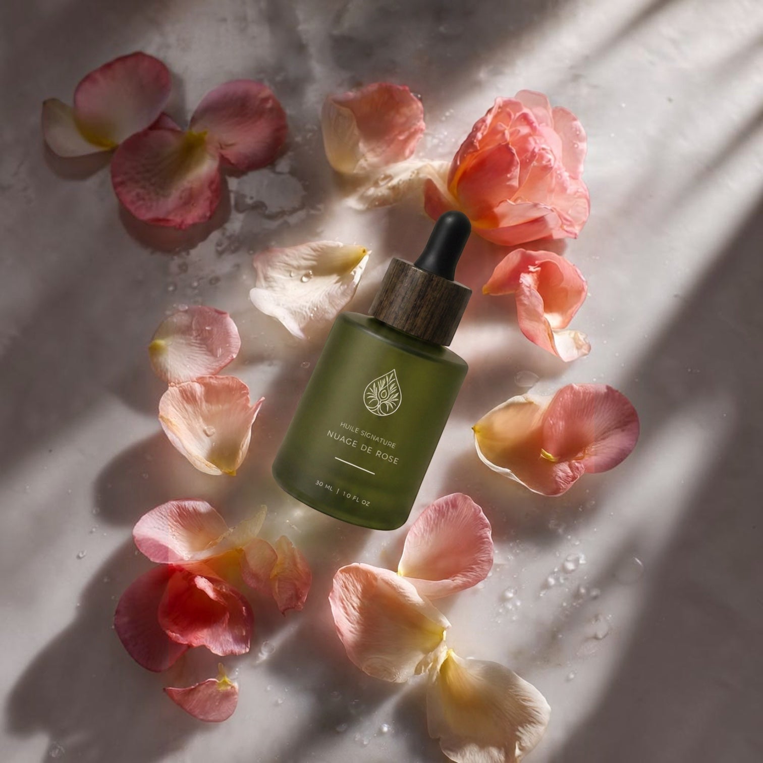 L'Arbre de paix Nuage de Rose signature oil in a green frosted glass bottle with a wooden dropper, surrounded by petals