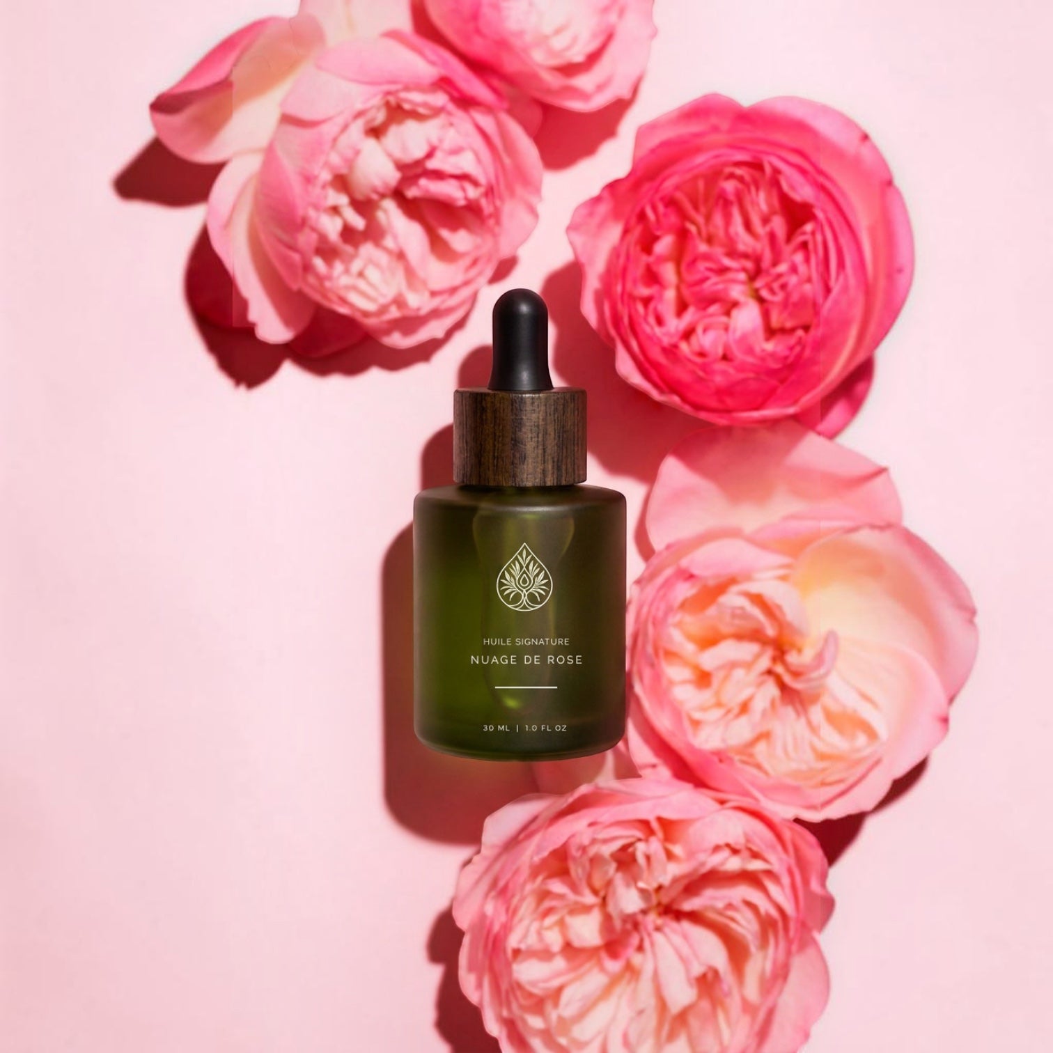 L'Arbre de paix Huile signature Nuage de Rose body oil in a green glass dropper bottle surrounded by pink roses.