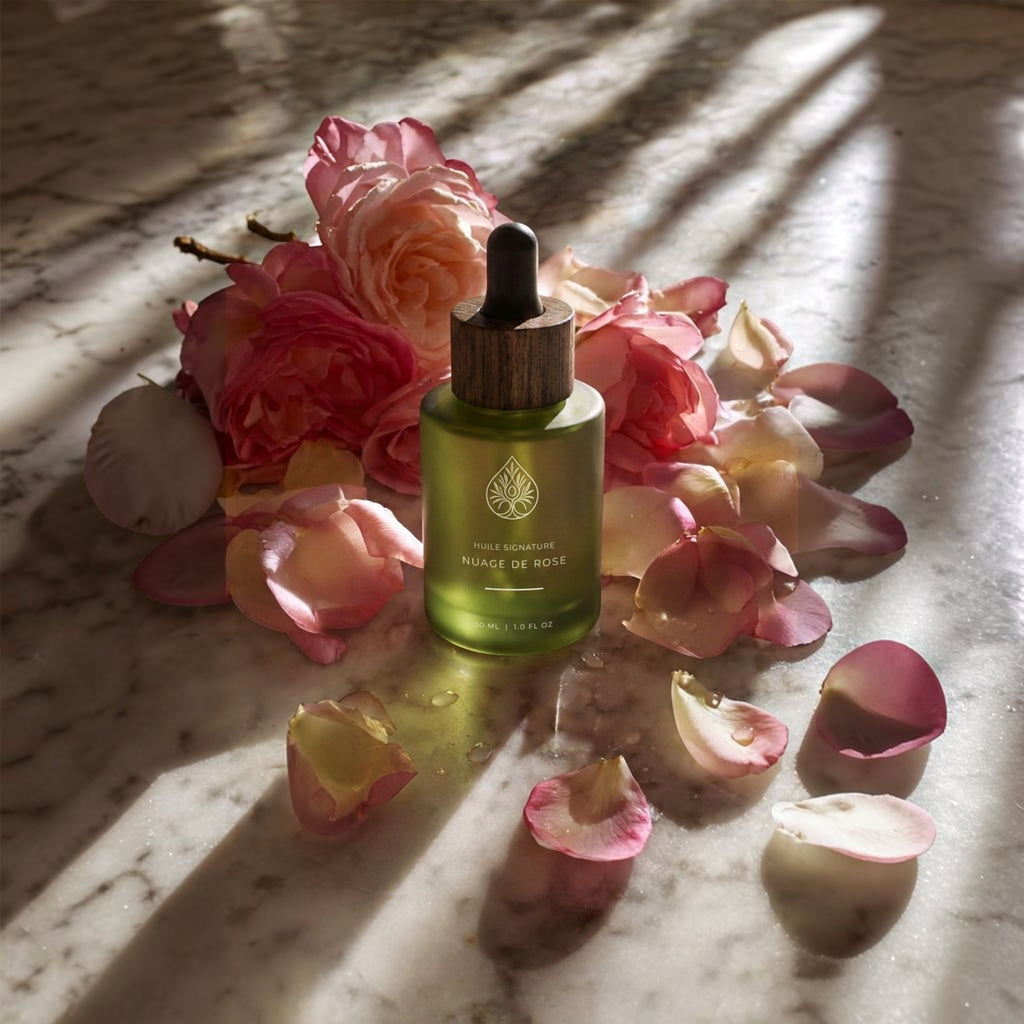 L'Arbre de paix Nuage de Rose signature oil in a frosted green glass bottle surrounded by fresh pink rose petals.