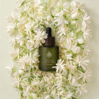L'Arbre de paix Nuit de Jasmin signature oil in a frosted green glass dropper bottle surrounded by fresh white flowers.