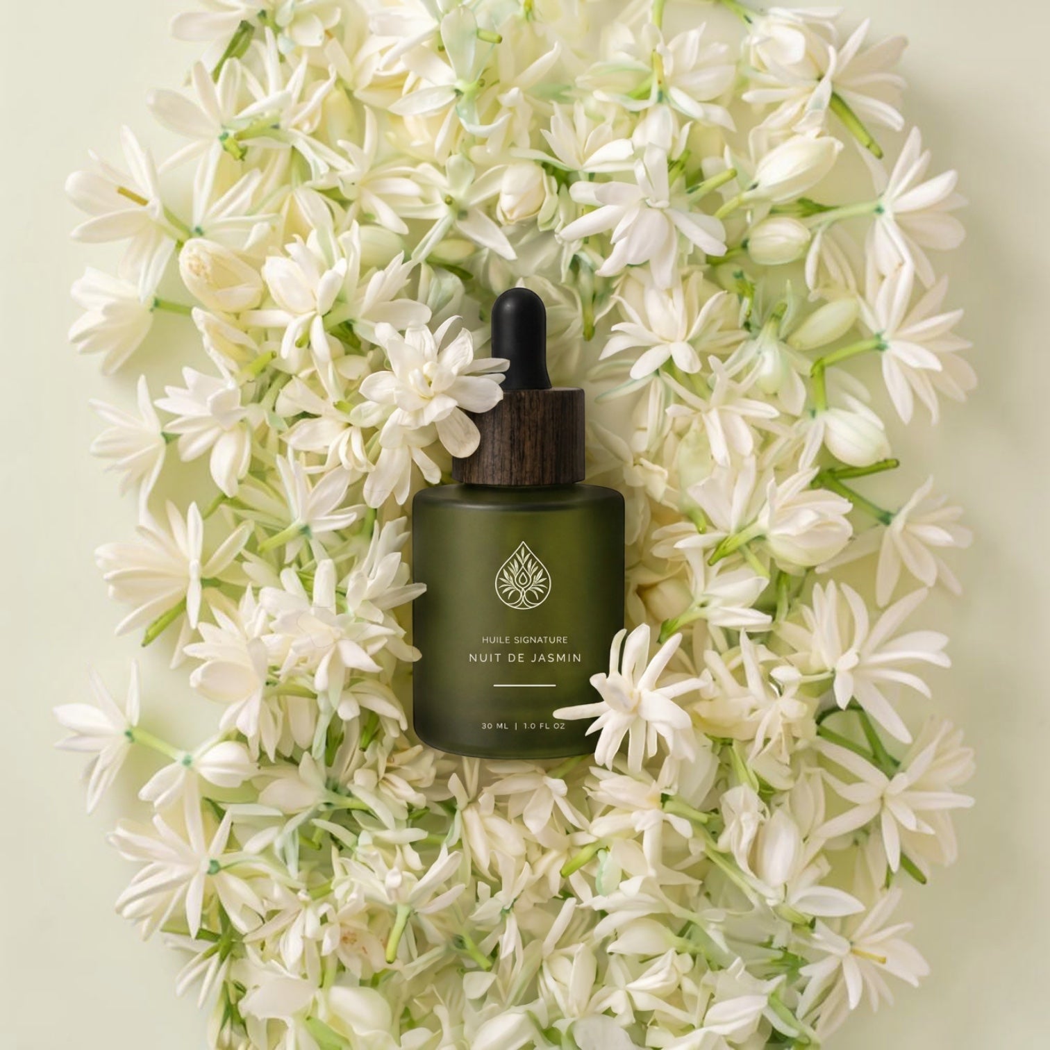 L'Arbre de paix Nuit de Jasmin signature oil in a frosted green glass dropper bottle surrounded by fresh white flowers.