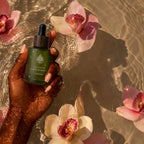 L'Arbre de paix Pureté Originelle signature oil in a green glass dropper bottle held in water with pink orchids