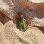 L'Arbre de paix Douceur d'Abricot signature oil in a green glass dropper bottle resting in warm beach sand