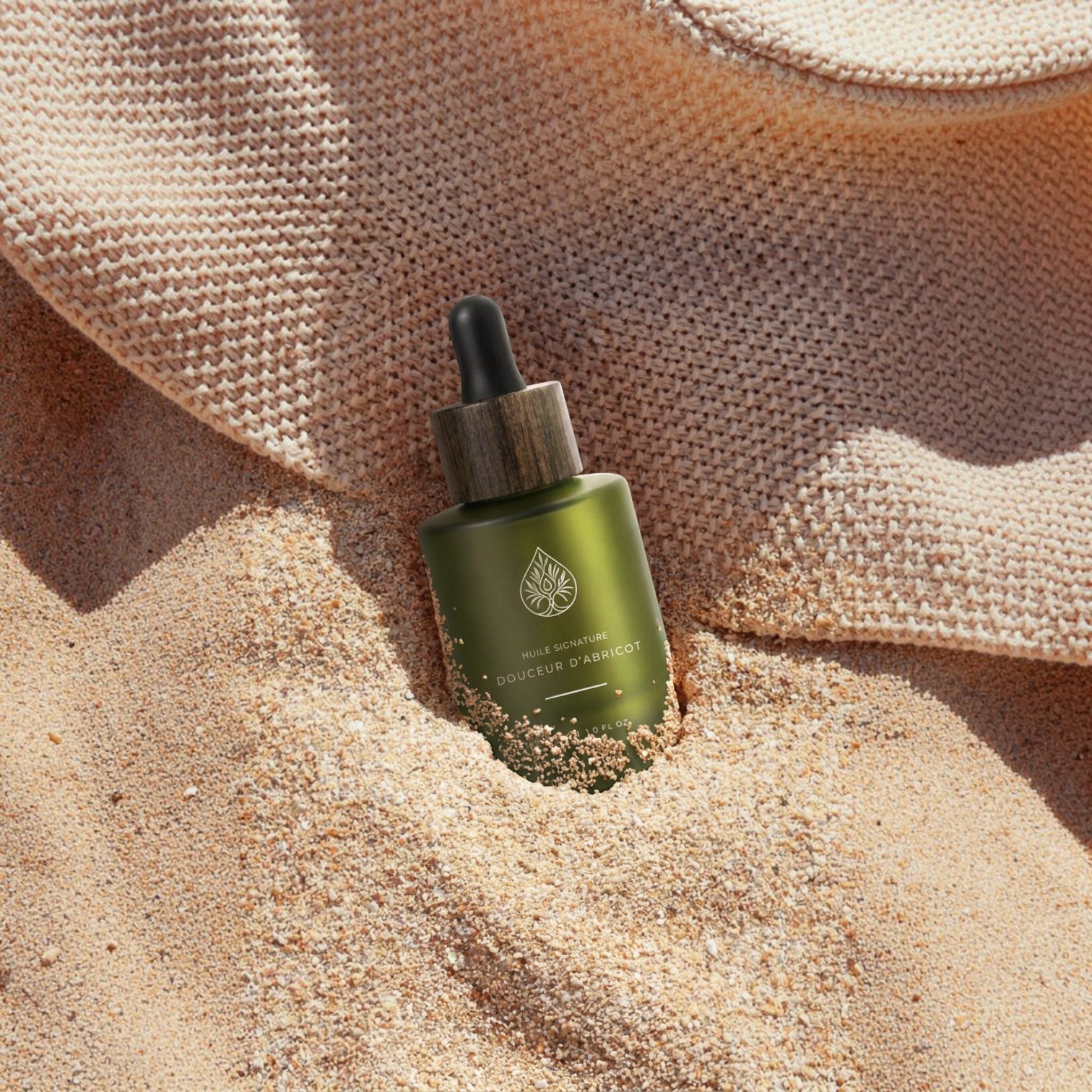 L'Arbre de paix Douceur d'Abricot signature oil in a green glass dropper bottle resting in warm beach sand